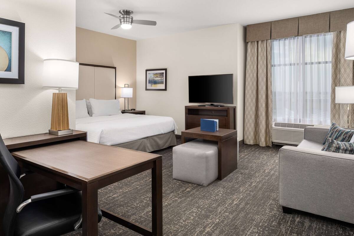Une chambre d’hôtel avec un lit, un bureau, une chaise, une télévision et un canapé.