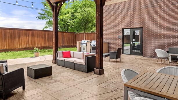 Une terrasse extérieure avec un mur en briques, un espace salon couvert avec un canapé et des fauteuils, et un coin barbecue.