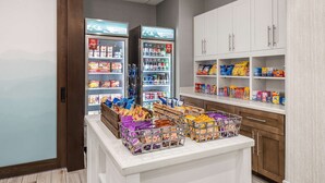 Un bar servant des collations, avec des boissons réfrigérées, des présentoirs de snacks et des étagères remplies de divers produits alimentaires.
