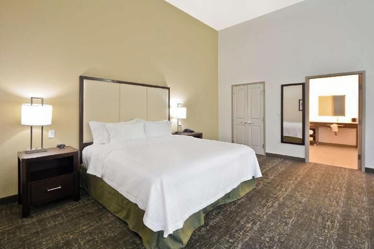 Una habitación de hotel con cama, mesitas de noche, un espejo y una puerta que da al baño.