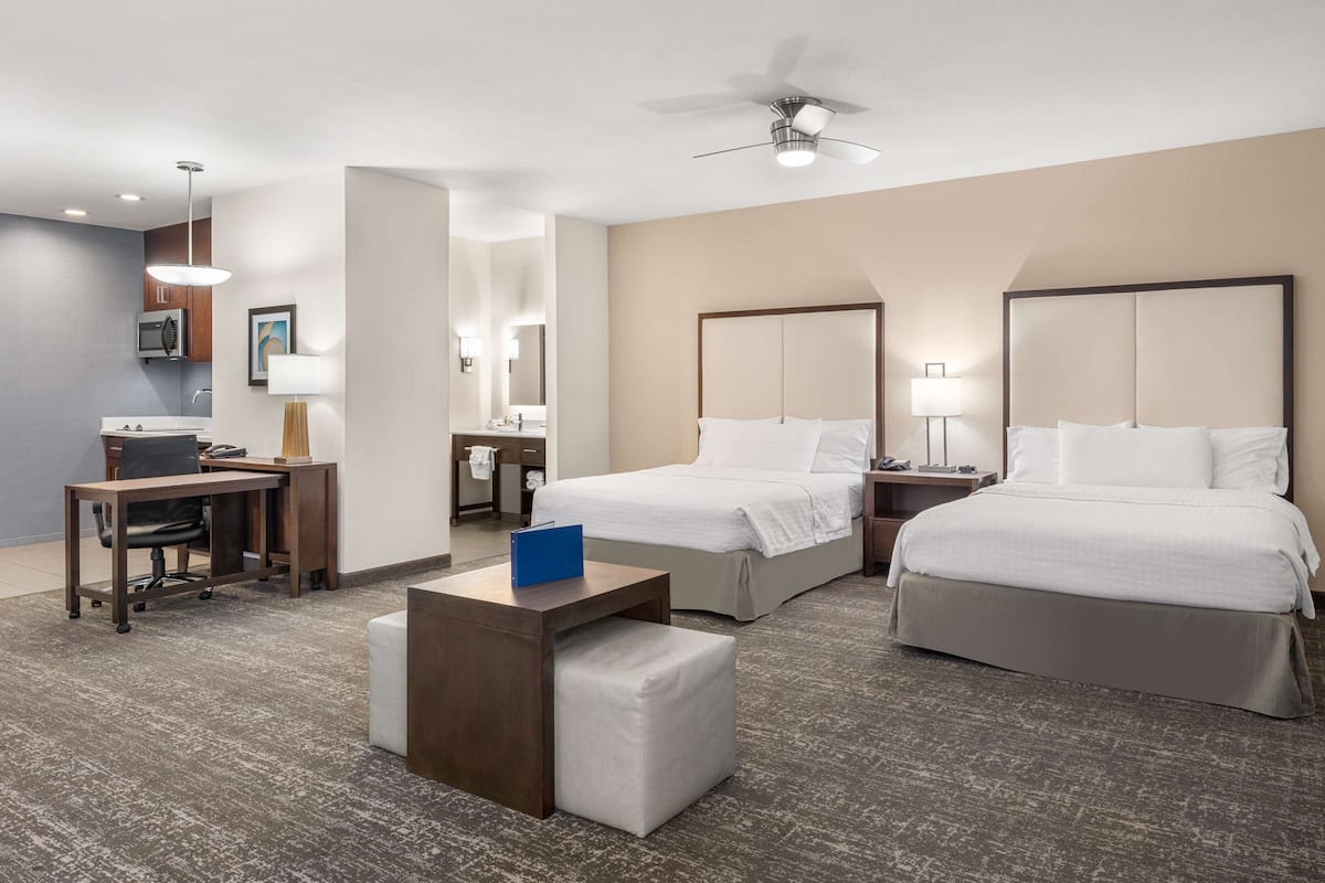 Une chambre d’hôtel avec deux lits, un bureau avec une chaise, une petite table et un ventilateur de plafond.