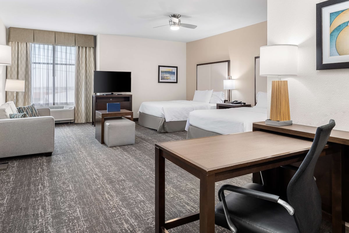 Une chambre d’hôtel équipée d’un lit, d’un bureau, d’une chaise, d’une télévision, d’une lampe et d’un ventilateur de plafond.