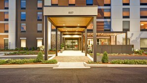A modern hotel entrance with a covered walkway, numbered 807, and a landscaped front garden. - Home2 Suites by Hilton Decatur Ingalls Harbor (Decatur)