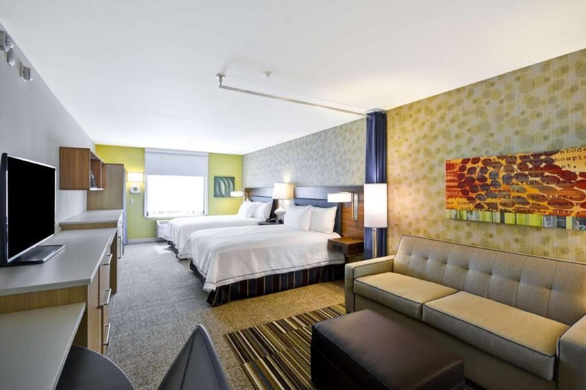 A hotel room with a bed, a sofa, a desk with a TV, and a wall with a patterned design.