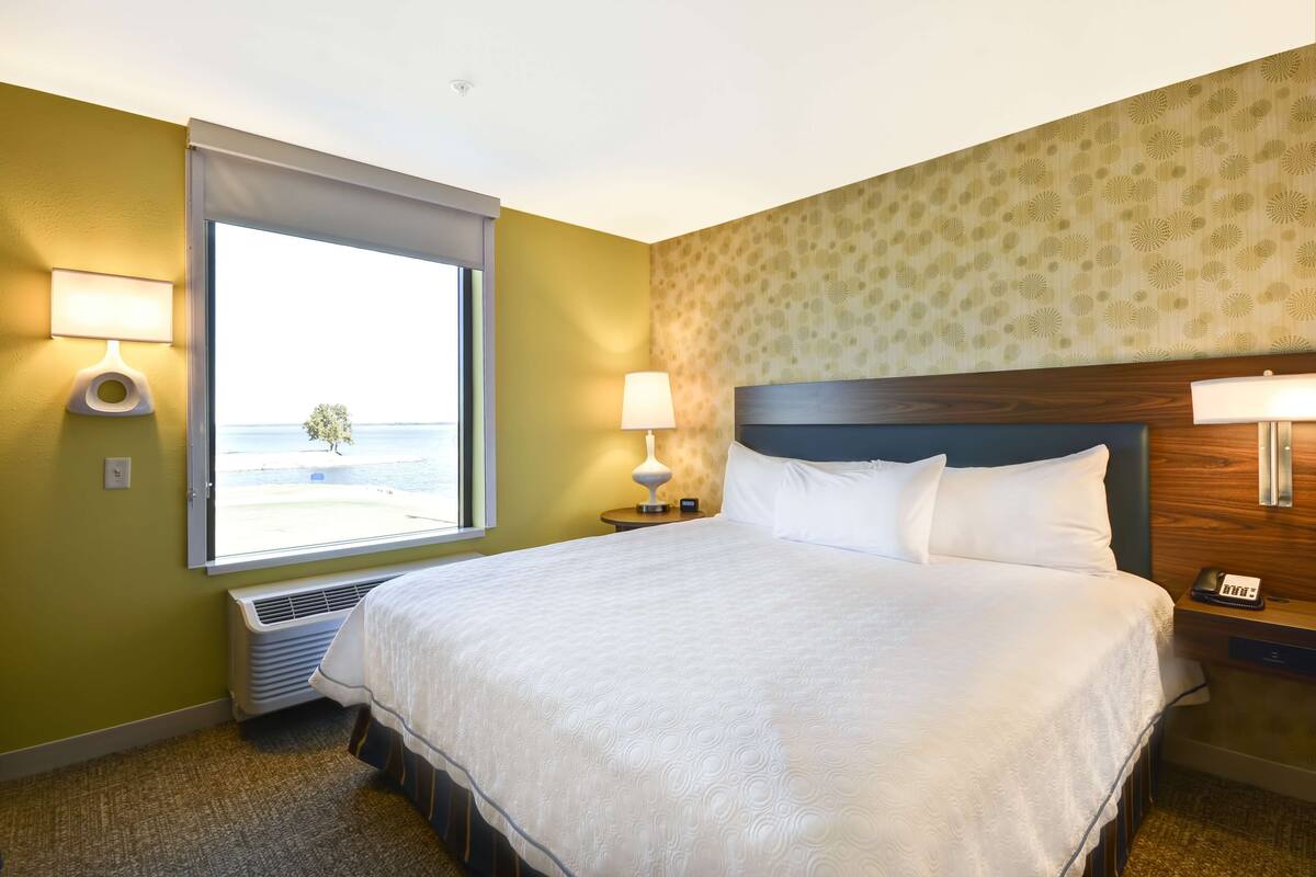 A hotel room with a large bed, two bedside lamps, a window with a view of the beach, and a wall with a floral pattern.