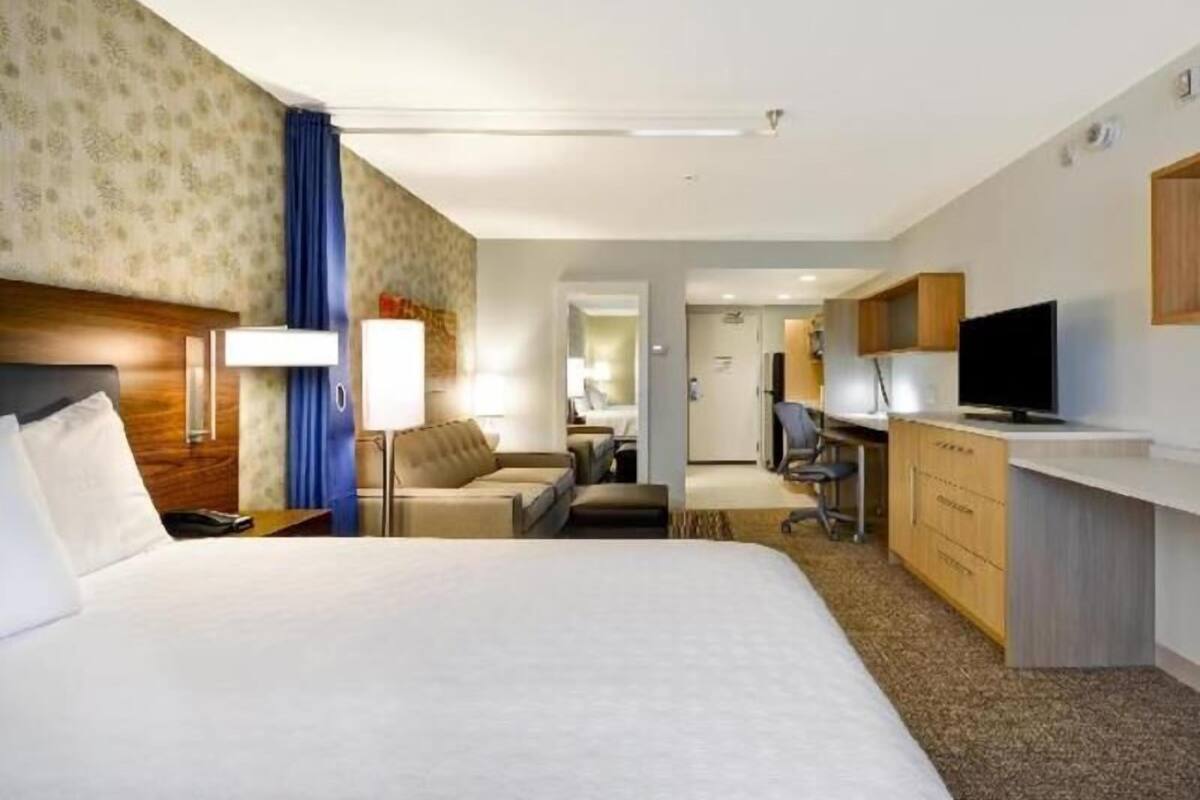 A hotel room with a large bed, a desk, a chair, a sofa, and a television.