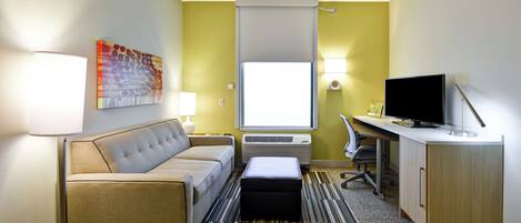 A hotel room with a sofa, a desk, a television, a lamp, an air conditioner, and a window with a view.