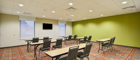 A conference room with a patterned carpet, multiple tables and chairs, a projector screen, and a green accent wall.