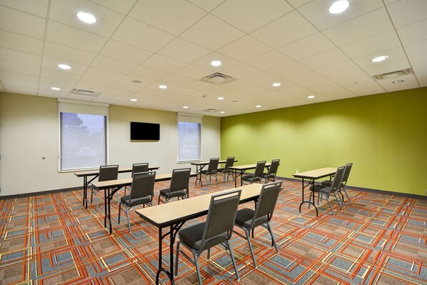 A conference room with a patterned carpet, multiple tables and chairs, a projector screen, and a green accent wall.