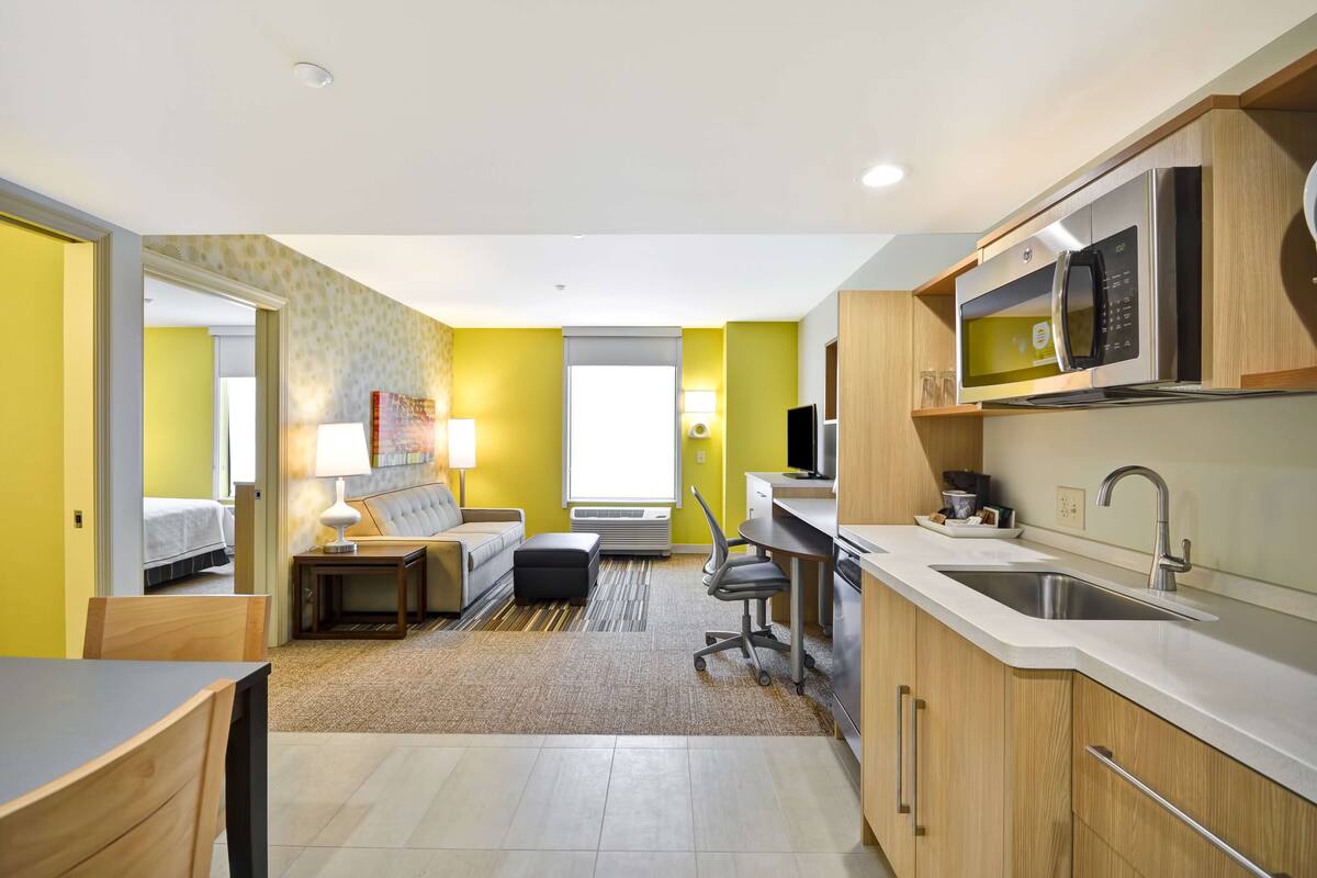 A compact hotel room with a kitchenette, a bed, a desk, and a sofa.