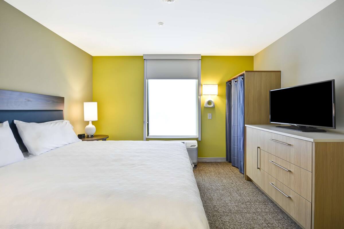 A hotel room with a bed, a TV, a nightstand, a lamp, a wardrobe, and a window with curtains.