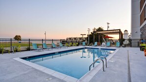 A rectangular swimming pool with a metal railing, surrounded by a low fence. There are several lounge chairs and a covered seating area with umbrellas. - Home2 Suites by Hilton Decatur Ingalls Harbor (Decatur)