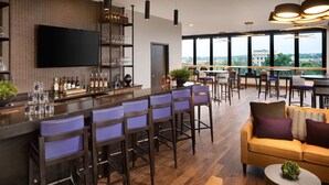 A modern bar area with a long counter, multiple bar stools, and a television mounted on the wall. - DoubleTree by Hilton Greeley at Lincoln Park (Greeley)