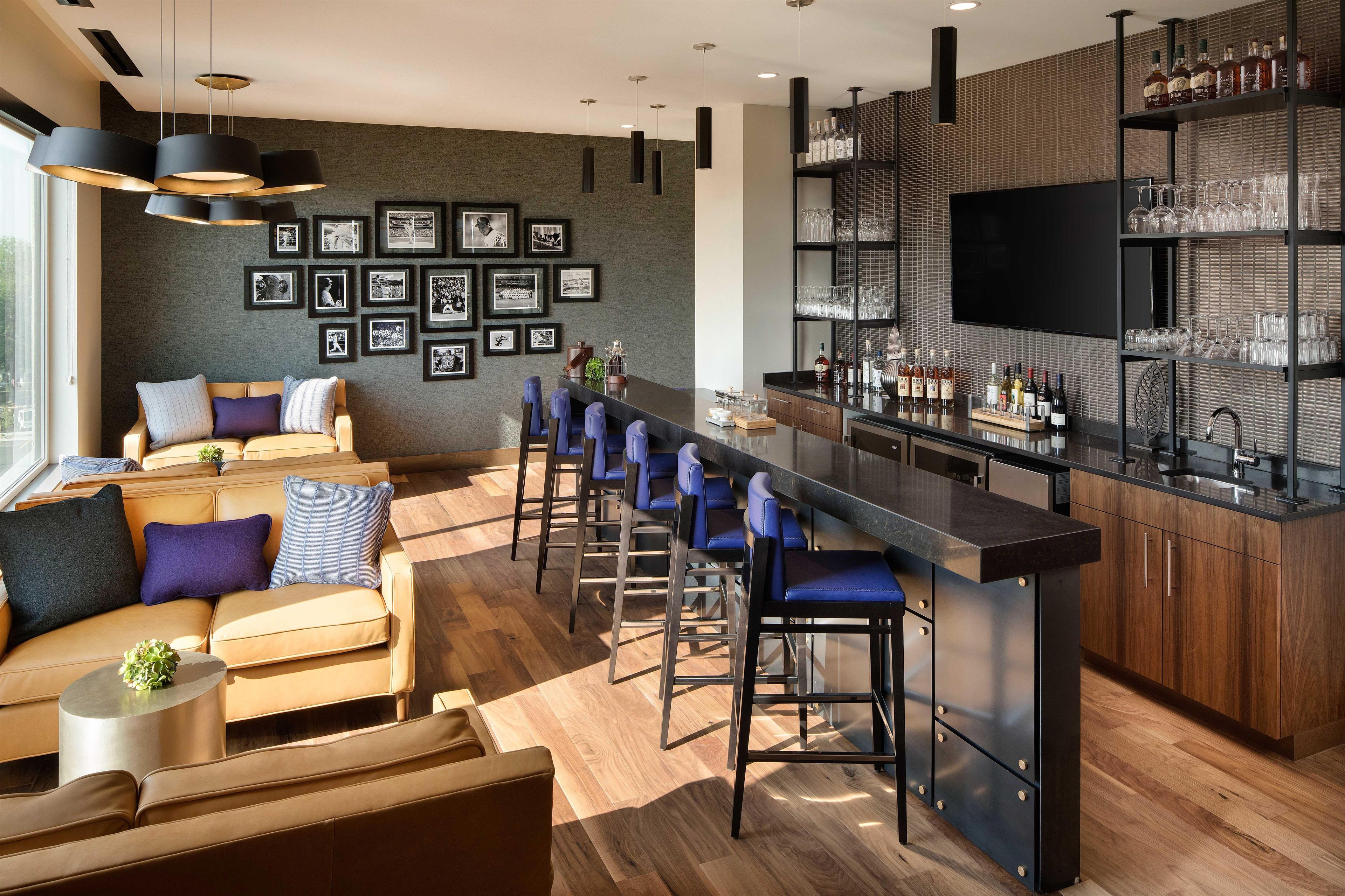 A modern bar area with a long counter, bar stools, and a television mounted on the wall.