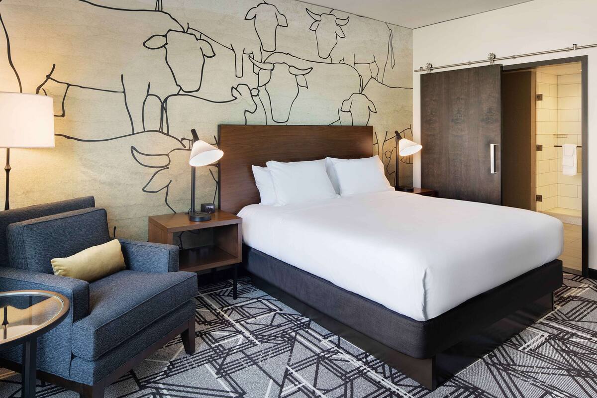 A hotel room with a large bed, a sofa, a nightstand, and a wall mural of cows.