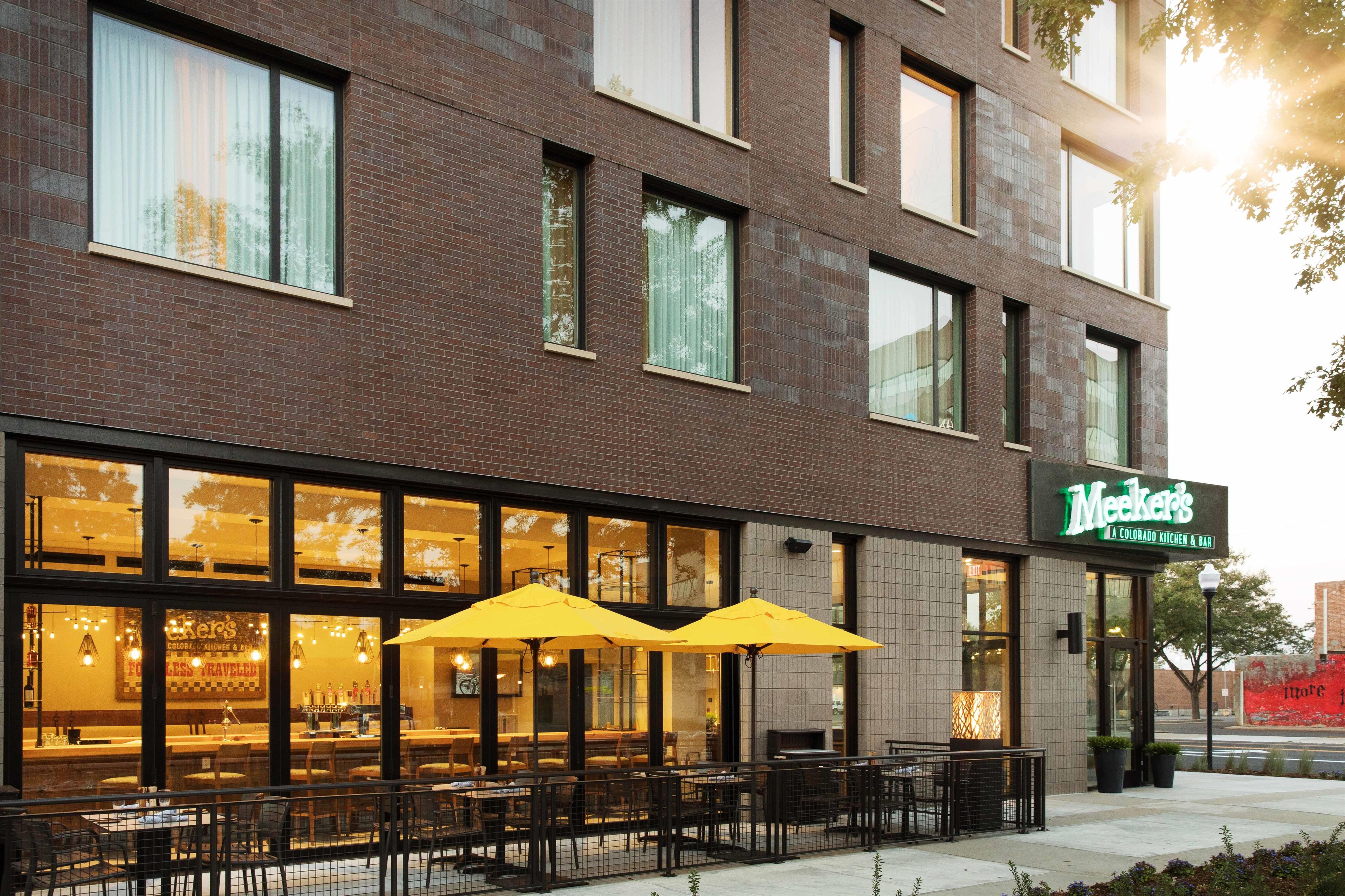 A brick building with large windows and outdoor seating with yellow umbrellas.