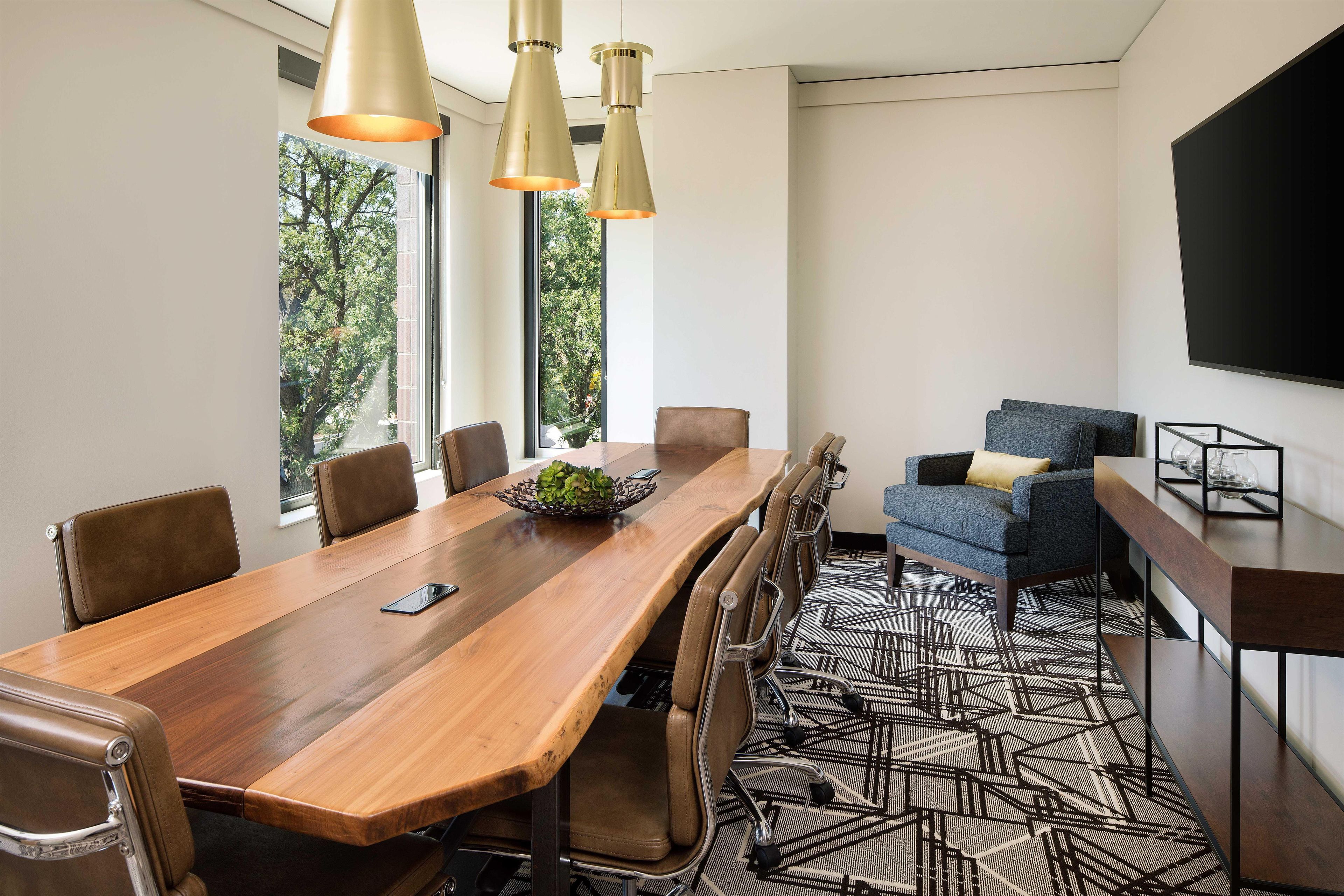 Un salón de conferencias con una larga mesa de madera, sillas de cuero, un sofá azul e iluminación colgante.