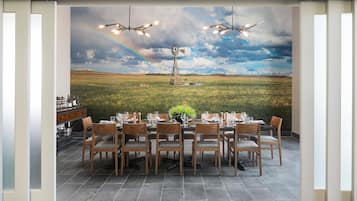 A dining area with a table set for six, chairs, and a view of a windmill and rainbow through a window.