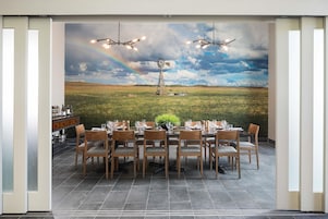 Comedor con una mesa dispuesta para seis personas, sillas y vistas a un molino de viento y un arcoíris a través de una ventana.