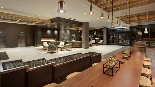 A modern hotel lobby with a central bar area, seating arrangements, and a large window providing a view of the outside. - DoubleTree by Hilton Greeley at Lincoln Park (Greeley)