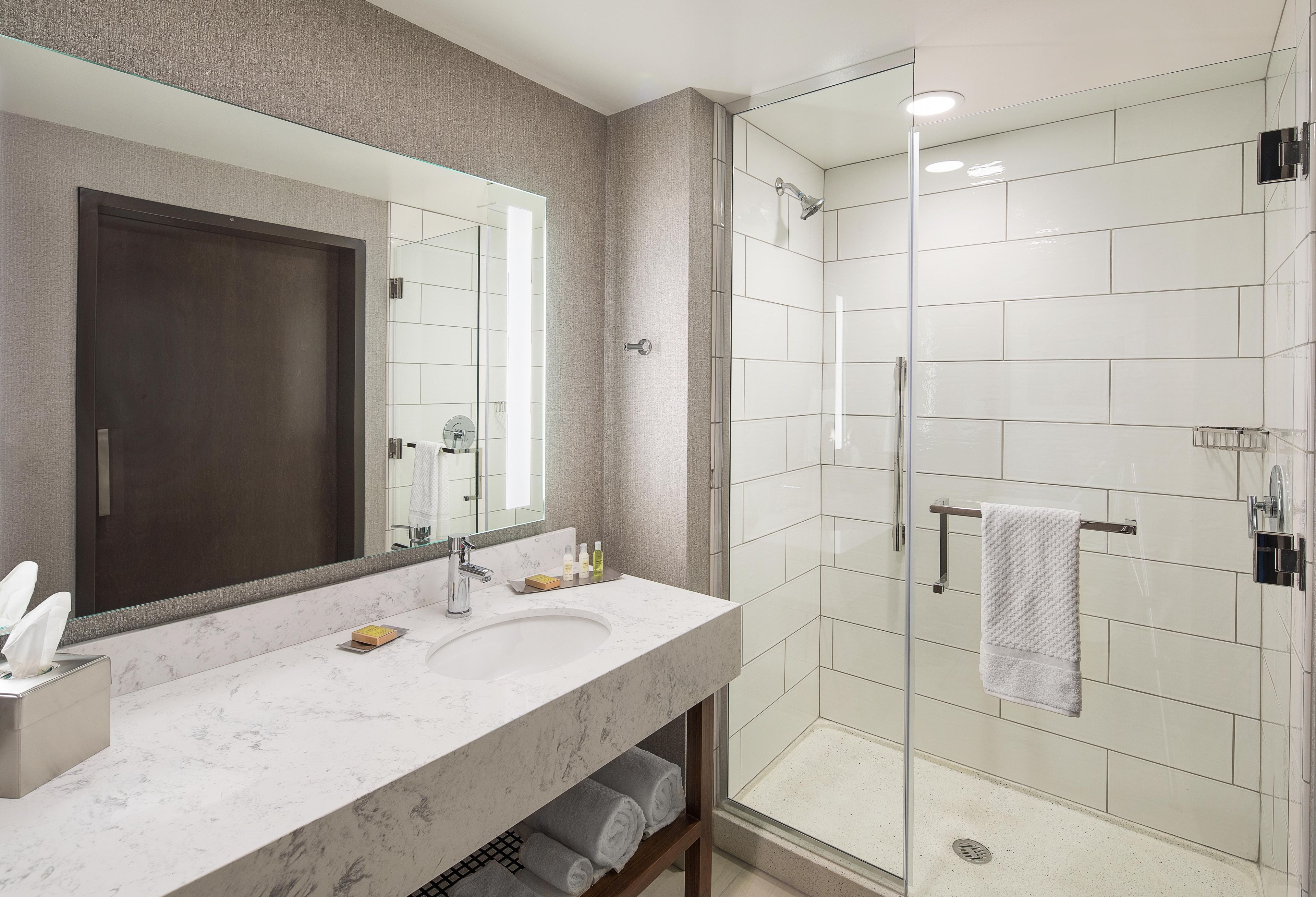 A modern bathroom with a large mirror, a sink, and a glass-enclosed shower.