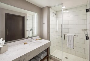 A modern bathroom with a large mirror, a sink, and a glass-enclosed shower. - DoubleTree by Hilton Greeley at Lincoln Park (Greeley)