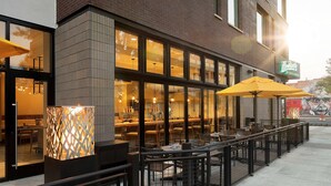An outdoor seating area with tables and chairs, a brick building facade, and a neon sign. - DoubleTree by Hilton Greeley at Lincoln Park (Greeley)