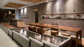 Un área de bar moderna con una larga barra de madera, varios taburetes y una fuente central.