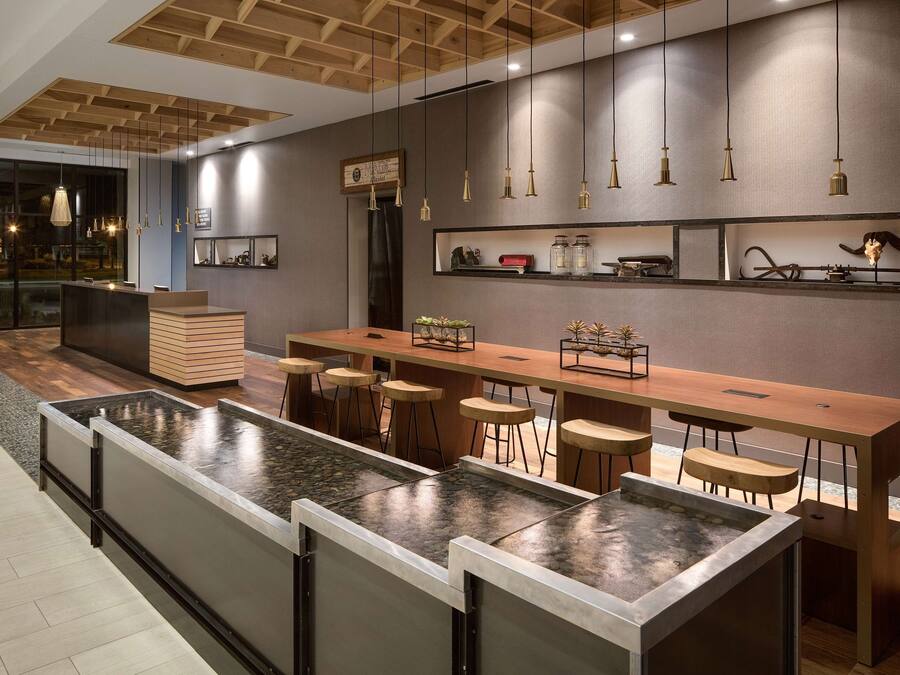 Un área de bar moderna con una larga barra de madera, varios taburetes y una fuente central.