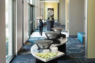 Un pasillo de hotel con mostrador de recepción, un camarero llevando bandejas y una mesa de buffet con platos y servilletas.