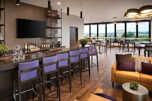 Un área de bar moderna con taburetes altos, un televisor de pantalla plana y vistas de la ciudad a través de amplios ventanales.