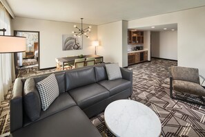 A modern living room with a sectional sofa, a round coffee table, and a dining area with a table and chairs. - DoubleTree by Hilton Greeley at Lincoln Park (Greeley)