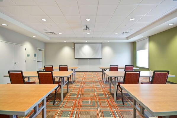 Un salón de conferencias con una pantalla grande, varias mesas y sillas.