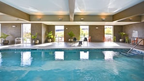 Una piscina interior con agua cristalina y paredes de azulejos, rodeada de amplios ventanales.
