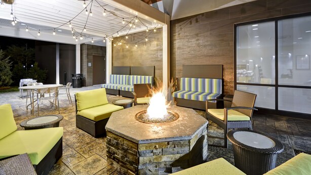 Un área de patio con un hogar a leña de piedra, muebles de mimbre e iluminación con luces colgantes.