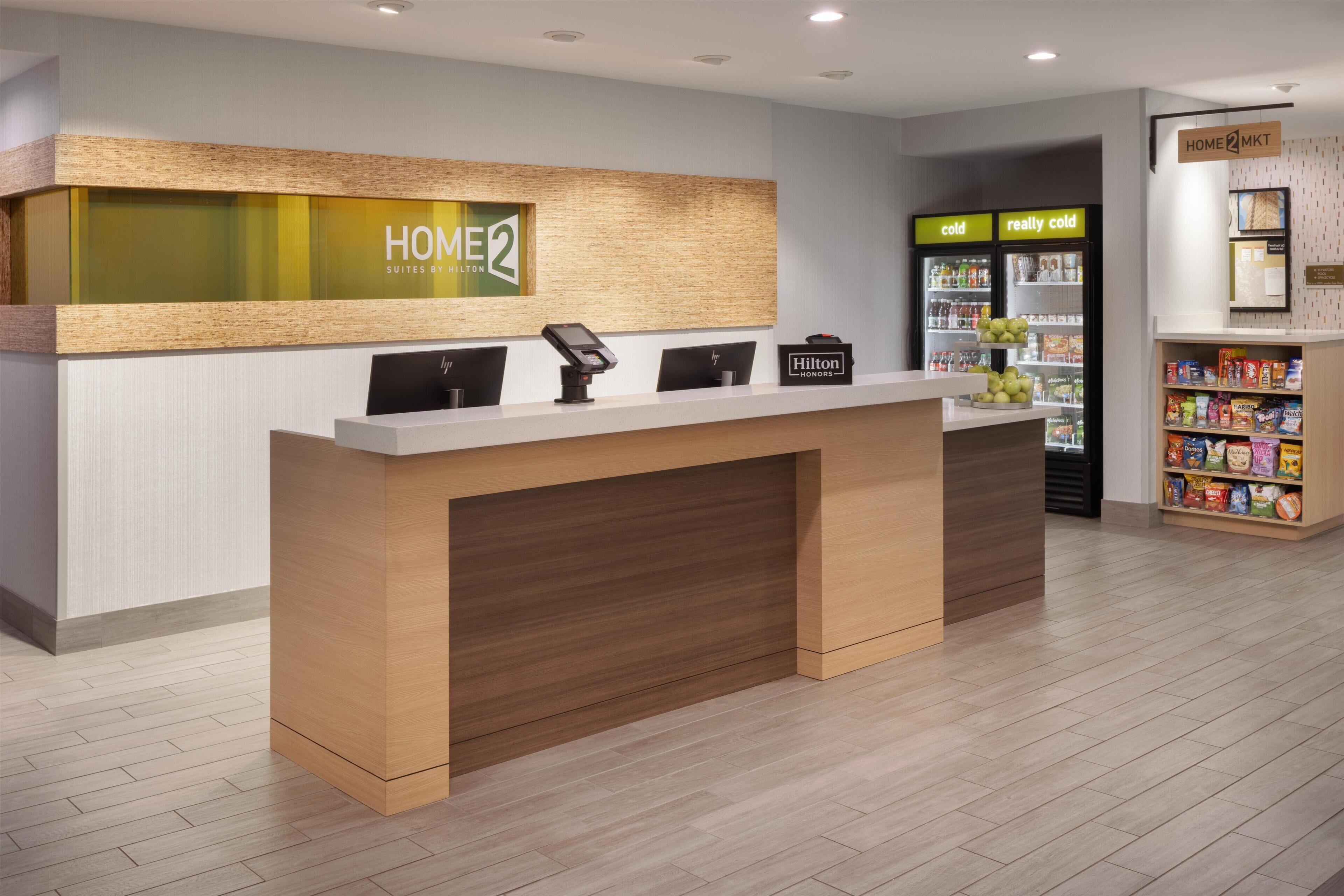 Un taulell de recepció d'hotel amb disseny modern, una estació de registre digital i una màquina de begudes automàtica.
