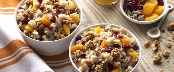 Three bowls of oatmeal with fruits and nuts on a wooden table.