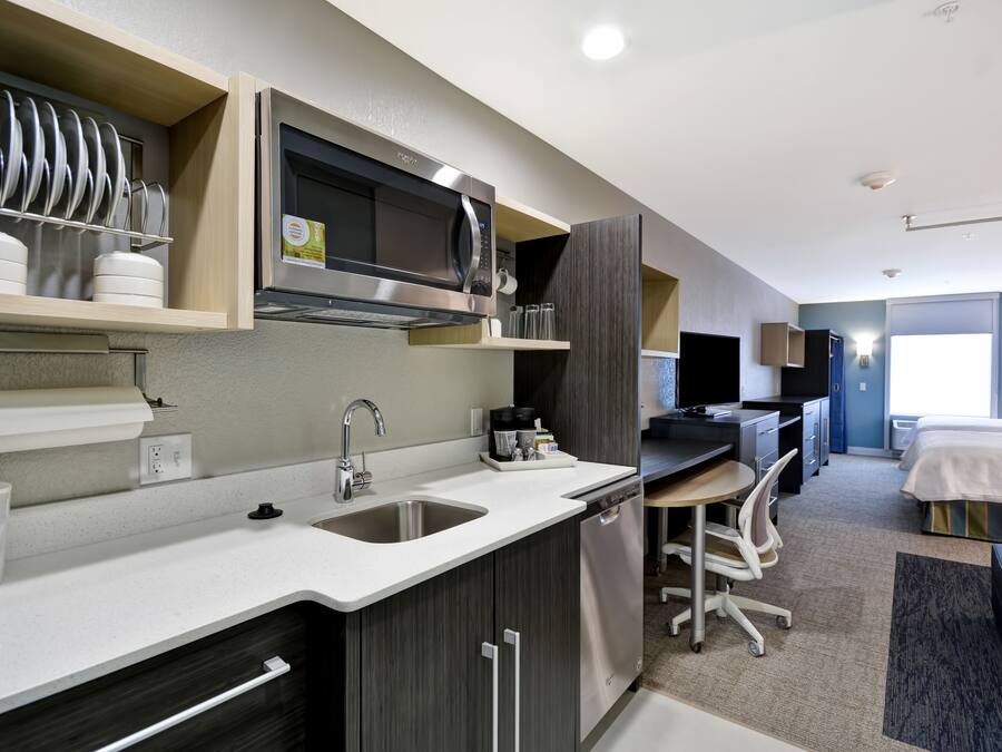 Una habitación de hotel compacta con kitchenette, una cama, un escritorio y una silla.