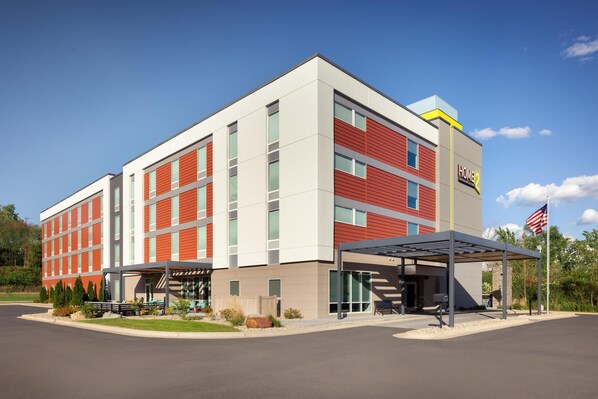 A modern hotel with a red and white facade, a covered entrance, and an American flag.