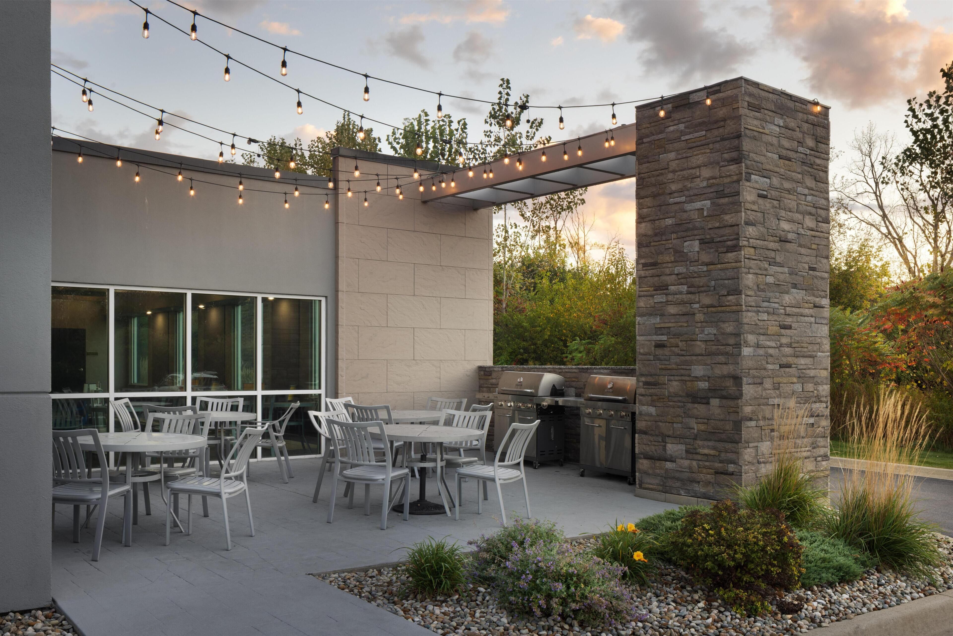 Un patio al aire libre con pared de piedra, una parrilla y luces colgantes.