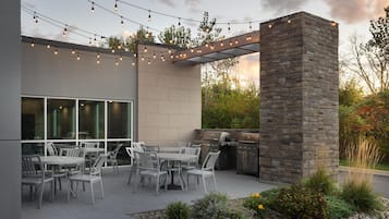 Un patio al aire libre con pared de piedra, una parrilla y luces colgantes.