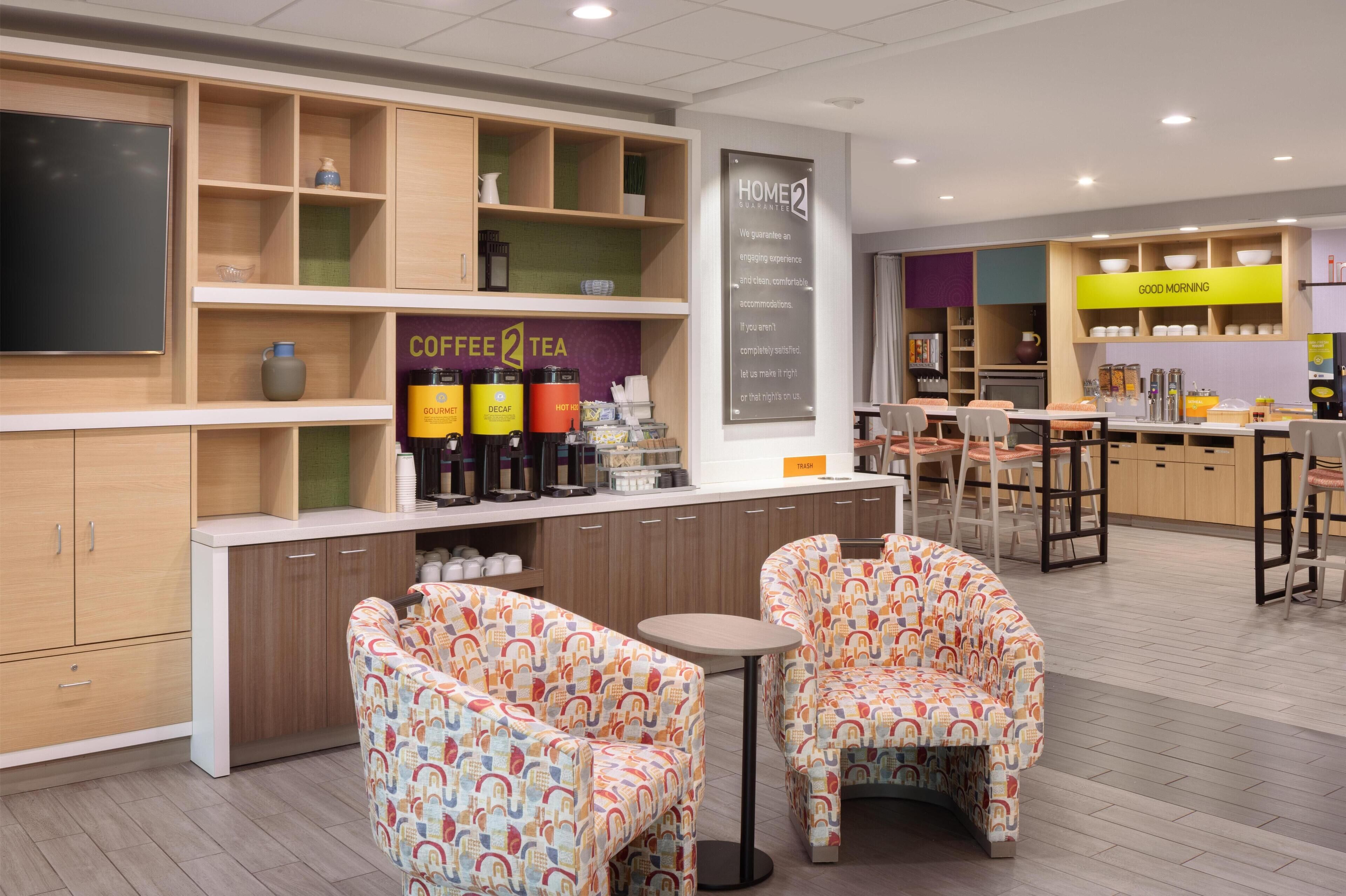 A modern cafe with a coffee and tea station, comfortable seating, and a 'Home2' sign.