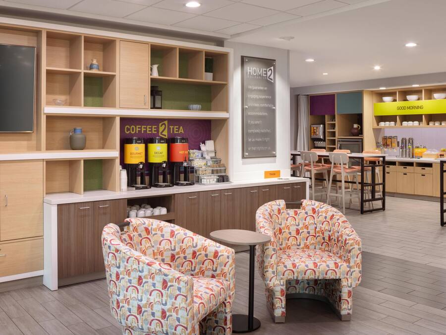 A modern cafe with a coffee and tea station, comfortable seating, and a 'Home2' sign.