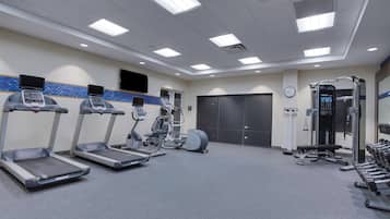 Un gimnasio con cintas de correr, elípticas, una banca para pesas y mancuernas.