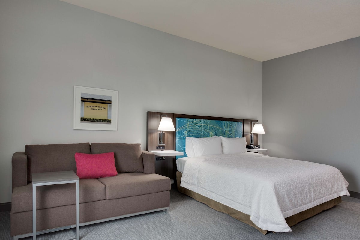 A hotel room with a bed, a sofa, a nightstand, and a framed picture on the wall.