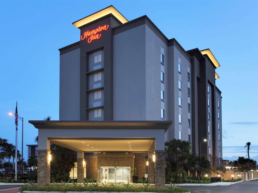 A Hampton Inn hotel with a modern design, featuring a prominent entrance and a clear sky in the background.
