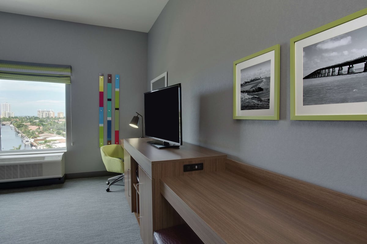 A modern office space with a large desk, a flat-screen TV, a chair, and a window with a city view.