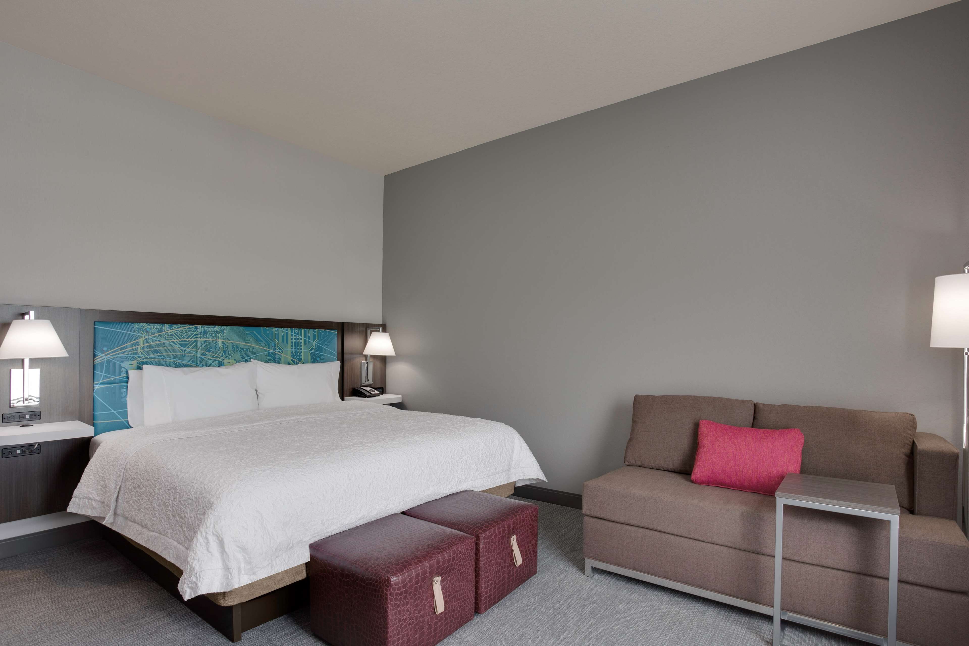 Quarto de hotel com uma cama, duas mesas de cabeceira com luminárias, um sofá com almofada e uma pequena mesa.