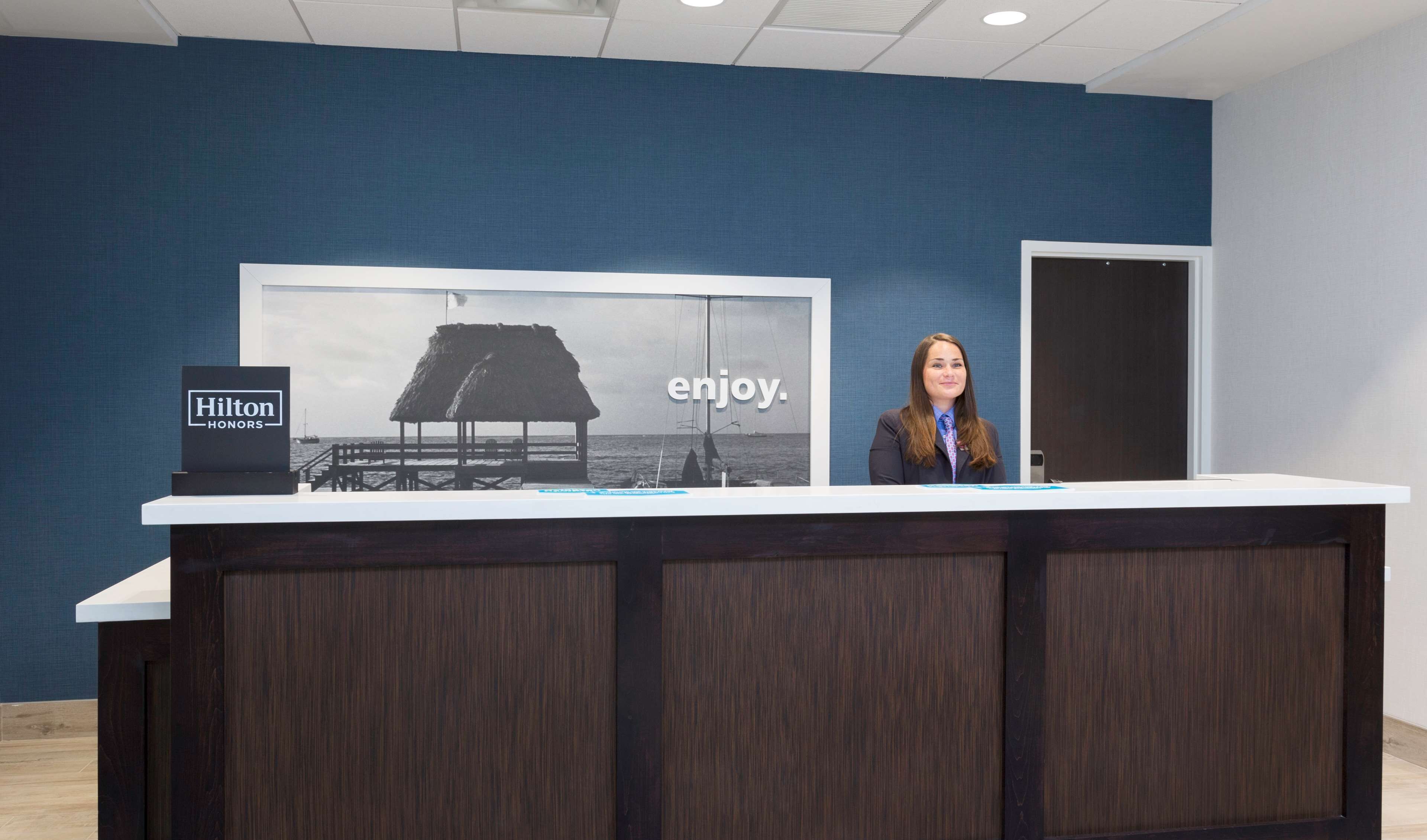 Una recepción con un letrero de Hilton Honors, un cartel grande con una escena de playa y la palabra "enjoy", y un acabado de madera oscura.