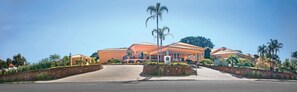 A large, orange villa with a stone wall entrance, a covered driveway, and a palm tree. - Vila Real Hotel (Jau)